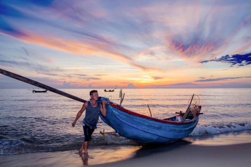 P&ecirc;cheur de Quảng B&igrave;nh, Vietnam, r&eacute;parant ses filets sur une plage au lever du soleil, illustrant la vie quotidienne des communaut&eacute;s de p&ecirc;cheurs locales
