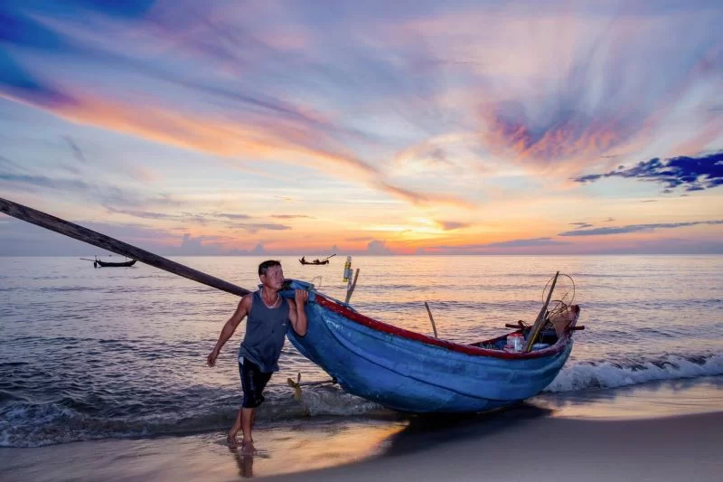 P&ecirc;cheur de Quảng B&igrave;nh, Vietnam, r&eacute;parant ses filets sur une plage au lever du soleil, illustrant la vie quotidienne des communaut&eacute;s de p&ecirc;cheurs locales